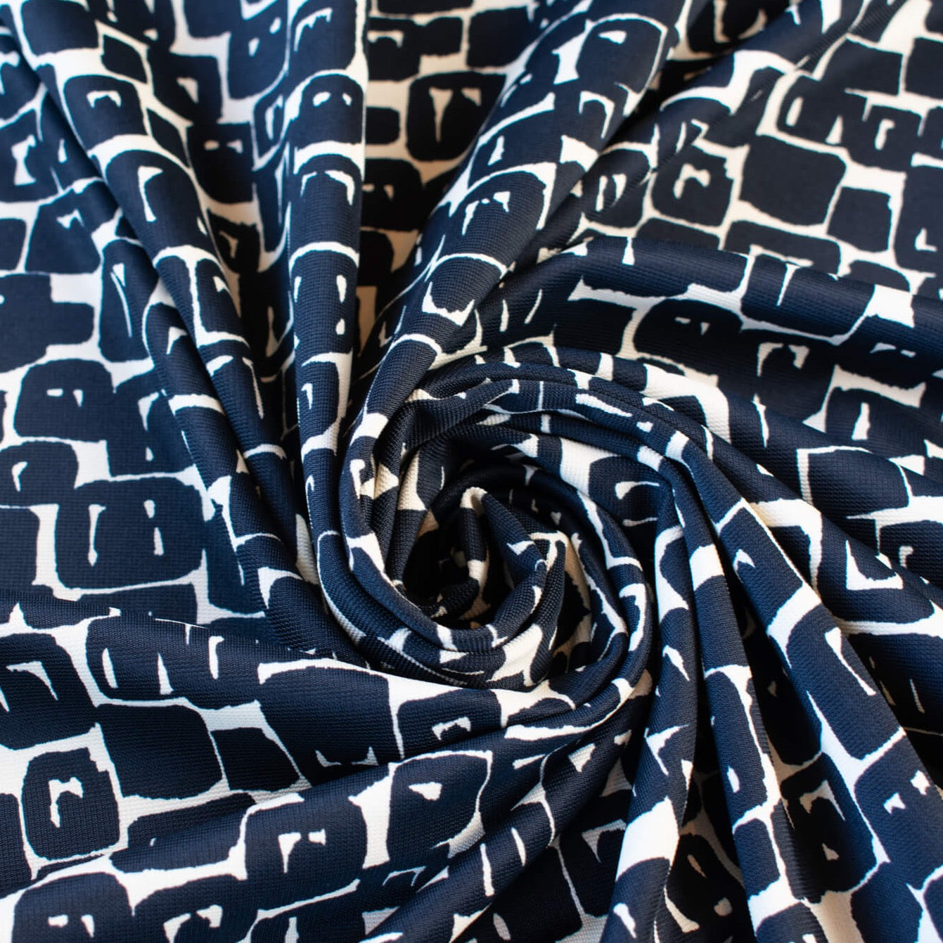 Designer Italian Matte Jersey Knit Fabric in a modern geometric print of abstract black squares se against a dark creme background - swirled to show fabric body  