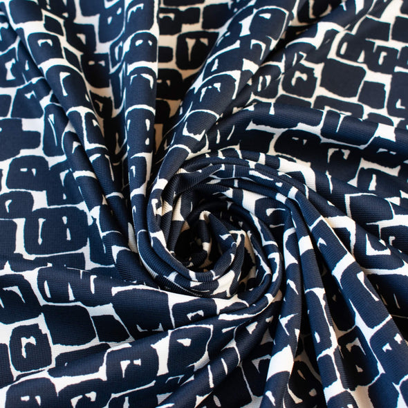 Designer Italian Matte Jersey Knit Fabric in a modern geometric print of abstract black squares se against a dark creme background - swirled to show fabric body  