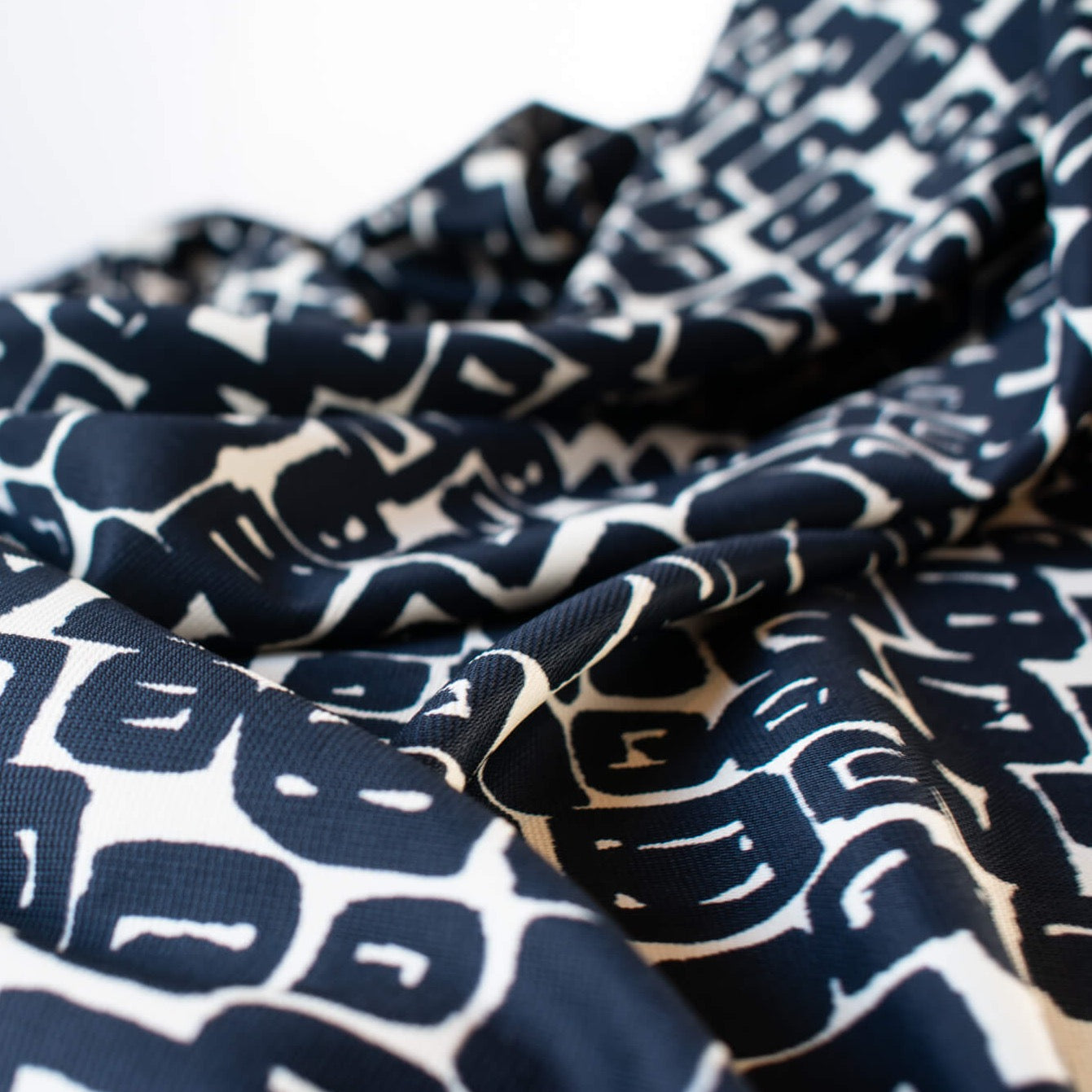 Designer Italian Matte Jersey Knit Fabric in a modern geometric print of abstract black squares se against a dark creme background - close up