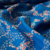 A stunning blue rayon floral challis will have you dreaming of summer strolls, taking in the sunshine and feeling so fine.  Soft and airy, perfect for lazy day dresses, billowy tops, or a simple cami and skirt.    Trailing light grey daises and red flowers with light turquoise leaves trail a delicate path against a medium blue background.   Close up image.