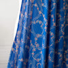 A stunning blue rayon floral challis will have you dreaming of summer strolls, taking in the sunshine and feeling so fine.  Soft and airy, perfect for lazy day dresses, billowy tops, or a simple cami and skirt.    Trailing light grey daises and red flowers with light turquoise leaves trail a delicate path against a medium blue background.   Image of fabric drape.