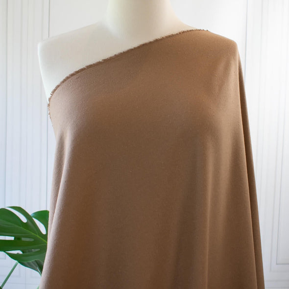 LA Designer silk noil in a soft creamy light carmel brown. A nice fabric for tailored and loose-fitting styles!  Perfect for a wide-leg pant, or a tailored shirt dress or a casual jumpsuit or jacket.    Silk noil has a moderate gentle drape, a soft, textured hand, and may have light or dark flecks. Image of fabric draped on mannequin.