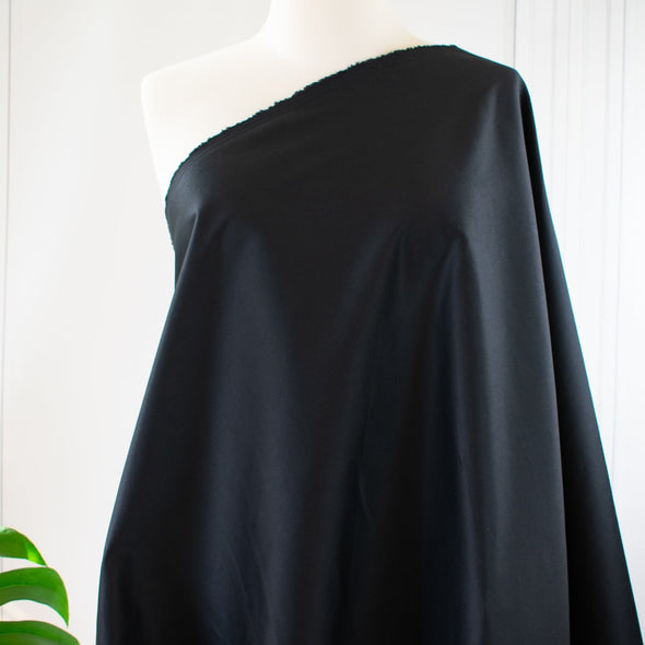 The lustrous sheen in this famous dress designer stretch sateen is a sure standout. In matte black, it has a smooth thin hand and will sew up a perfect year round garment. Opaque and a bit of stretch, not only will you look stunning but it's comfortable too! Image of fabric draped on dress form.