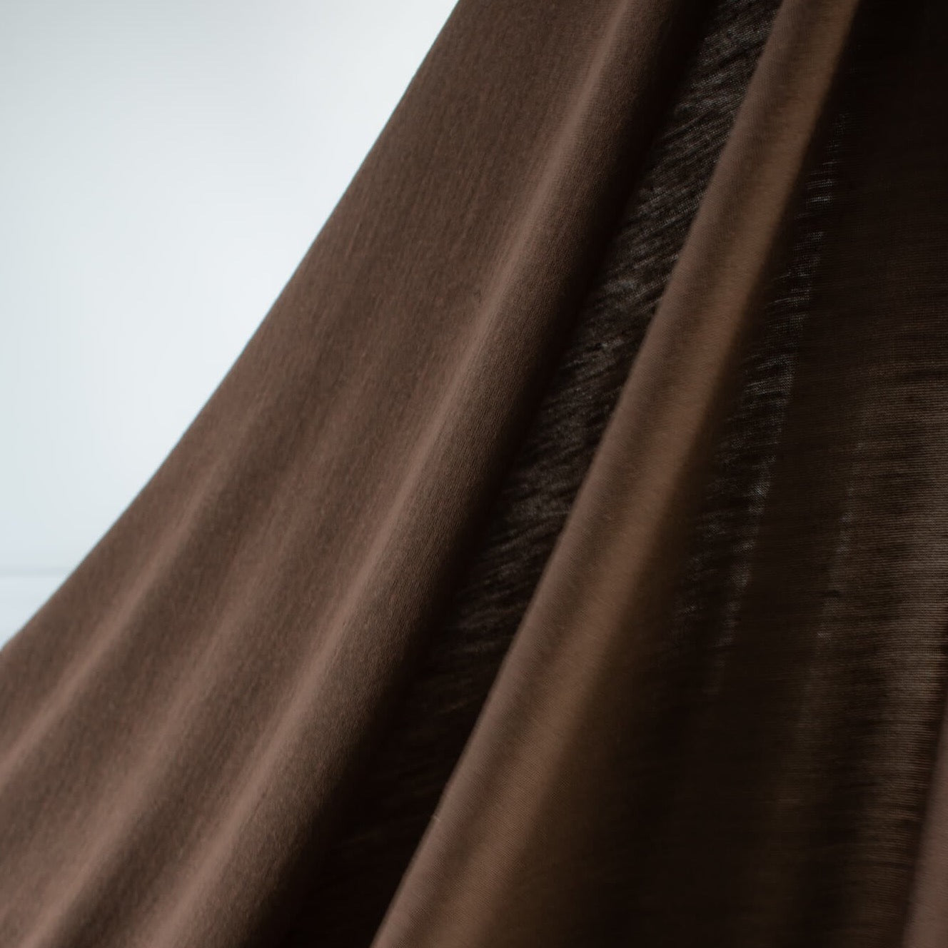 Merino Wool Jersey knit in a gorgeous chocolate brown.   This fabric has a soft hand and is light and flowy, perfect for a top or cardigan. It makes a perfect layering piece. A generous width at 63 inches and a mechanical stretch.  Image of fabric drape.