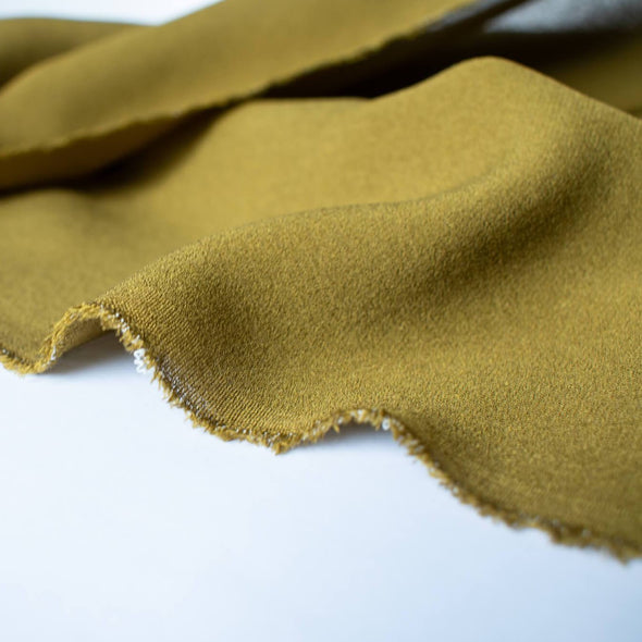 NYC Designer Couture silk crepe de chine in a fantastic width. This mustard green color will bring any of your neutrals a great pop of color! Photo of selvedge.
