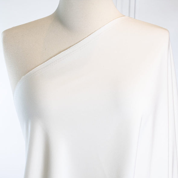 Power Suiting never felt so good!  NYC designer fine twill is a soft touch with a semi-textured hand. Not only is it in an easy to care for poly/lycra blend but it has a bit of stretch for comfort. This fine suiting is an opaque soft powder white that flatters!   Close up on dressform.